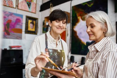 Two women, painting together in an art studio. clipart