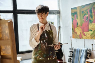 Woman in art studio creating with paintbrush. clipart