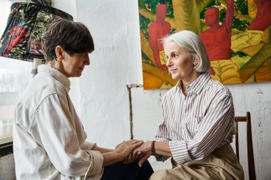 Mature lesbian couple admiring a painting together in art studio. clipart