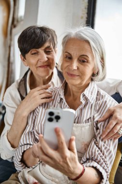 İki kadın fotoğraf çekmek için akıllı telefon kullanıyor.