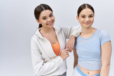 Two pretty, young brunettes in sportswear standing side by side, showing friendship and confidence. clipart