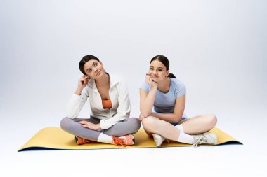 İki güzel, esmer genç kız spor kıyafetleri içinde yoga minderinde oturup bir an rahatlama ve iletişim kuruyorlar..