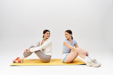 Spor kıyafetli iki güzel, esmer genç kız stüdyoda yoga minderinde otururken huzurlu bir anı paylaşıyorlar..