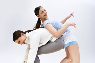 Two pretty, brunette teenage girls in sportive attire show off their dance moves in a studio against a grey background. clipart