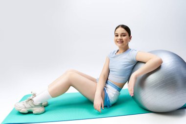Güzel, esmer, spor elbiseli bir kız stüdyo ortamında bir spor salonunun tepesinde zarifçe oturuyor.