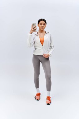 Spor kıyafetli esmer bir kız stüdyo ortamında cep telefonuyla selfie çekiyor..