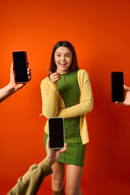 A young girl in a green dress standing confidently near many cell phones clipart