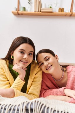 Two pretty teenage girls dressed casually, lying side by side on a bed, enjoying a moment of peaceful togetherness. clipart