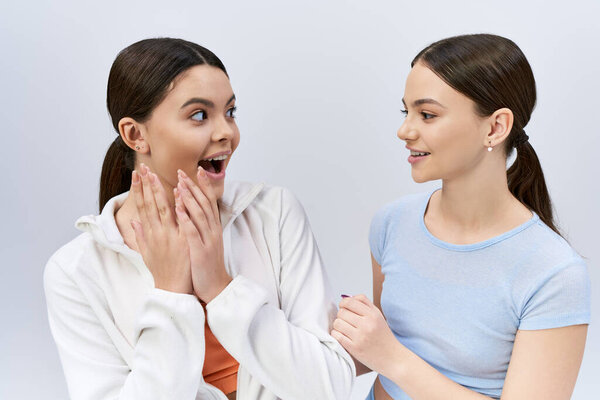 Two young teens in sportswear laughing on a grey studio background.