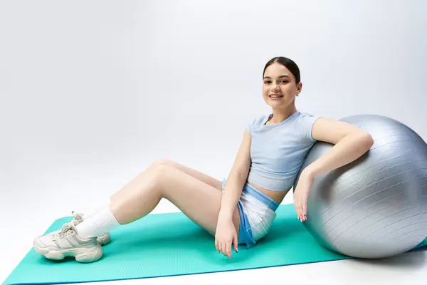 stock image A pretty, brunette girl in sportive attire sits gracefully on top of a gym ball in a studio setting