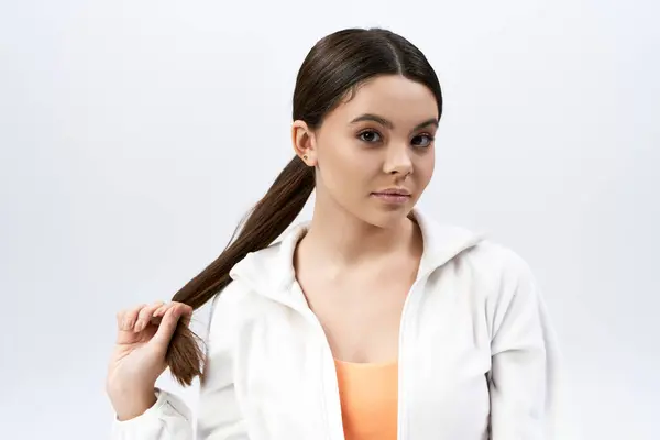 stock image A brunette teenage girl with a ponytail wearing sportive attire against a grey studio backdrop.