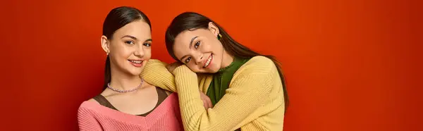stock image Two pretty, brunette teenage girls stand side by side in front of a vivid red wall, exuding friendship and confidence.
