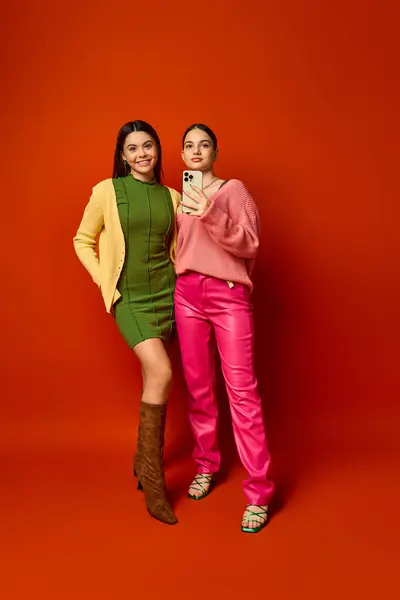 stock image Two pretty teenage brunettes in casual attire stand together in front of a vibrant red background.