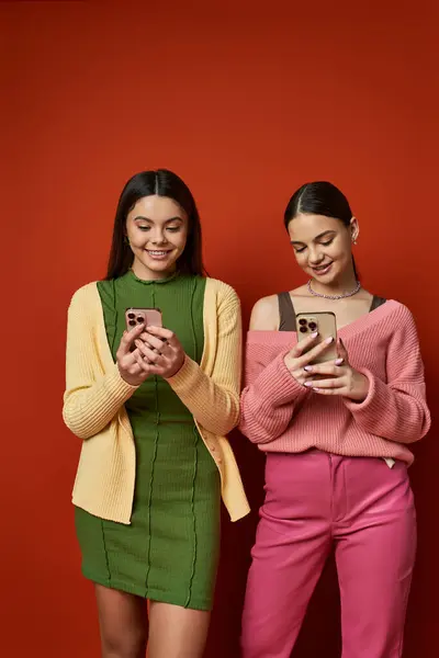 stock image Two pretty brunette teenage girls in casual attire, standing next to each other, holding cell phones, and smiling.