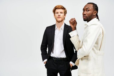 Two handsome, multicultural men in elegant attire stand together against a white background. clipart