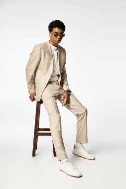 Handsome African American man in tan suit sitting on stool with stylish sunglasses. clipart