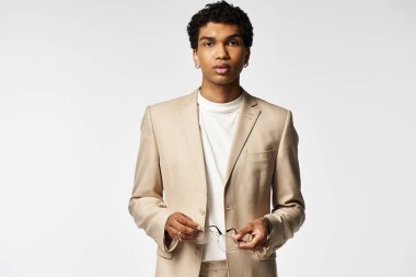 Şık güneş gözlüklü yakışıklı Afro-Amerikan adam bronz bir takım elbise içinde rahatça poz veriyor..