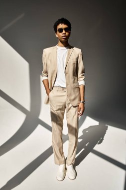 Handsome African American man in beige suit and stylish sunglasses standing in front of white wall. clipart