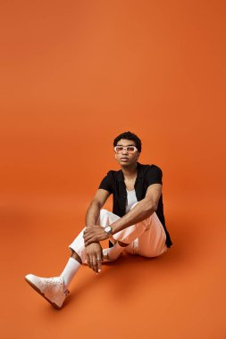 Güneş gözlüklü yakışıklı adam canlı turuncu arka planda oturuyor..