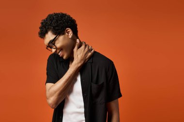 Gözlüklü ve siyah gömlekli yakışıklı adam turuncu arka planda poz veriyor..