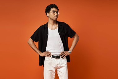 Beyaz kot pantolon ve siyah gömlek giyen, şık güneş gözlüğü takan yakışıklı Afro-Amerikan bir adam..