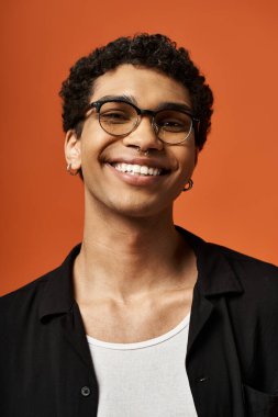 Zarif gözlüklü yakışıklı bir Afrikalı Amerikalı parlak turuncu bir fona gülümsüyor..