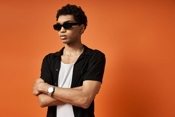 Handsome African American man in stylish sunglasses against bright orange backdrop.
