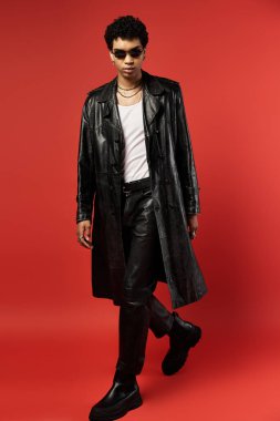 Trençkotlu yakışıklı Afro-Amerikalı adam canlı kırmızı arka planda poz veriyor..