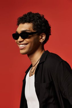 Şık güneş gözlüklü yakışıklı Afro-Amerikan adam canlı kırmızı bir arka plana gülümsüyor..