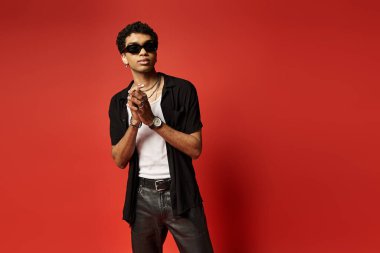 Handsome African American man in sunglasses striking a pose against a vibrant red backdrop. clipart