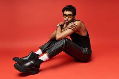 Kırmızı arka planda oturan, güneş gözlüklü Afrikalı Amerikalı bir adam..