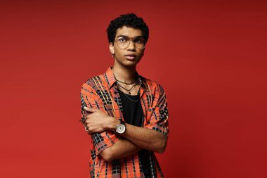 Handsome young man posing confidently in plaid shirt against vibrant red backdrop. clipart