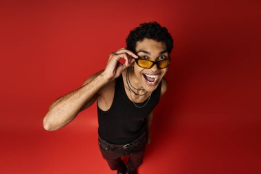 Parlak kırmızı arka planda güneş gözlüğü takan yakışıklı Afro-Amerikan bir adam..
