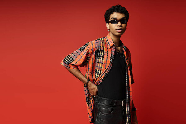 Handsome African American man in plaid shirt and leather pants poses on vibrant red background.