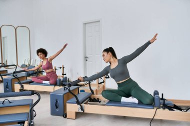 Two women gracefully execute exercises in a gym setting. clipart