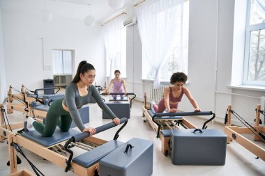 Çeşitli kadınlar pilates kursuna gidiyor, güç ve esneklik egzersizlerine odaklanıyor..