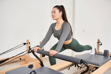Gri gömlekli, yeşil pantolonlu, pilates dersinde spor yapan bir kadın..