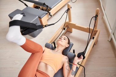 Spor bir kadın pilates dersi sırasında sabit bir egzersiz makinesinin üzerinde yatıyor..