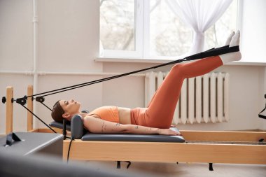 Turuncu bluzlu bir kadın egzersiz yapar, güç ve kararlılık gösterir..