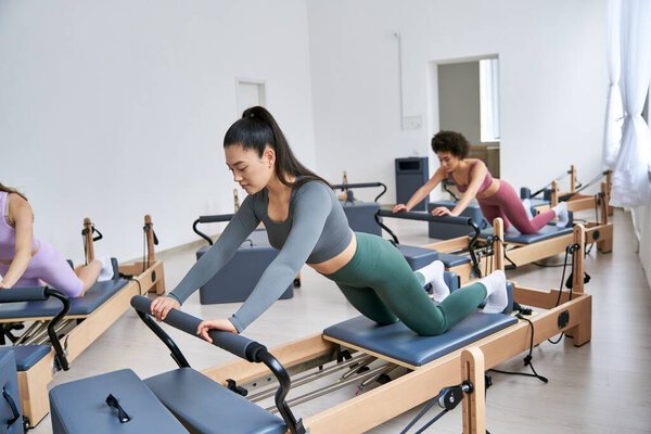 Women engage in pilates class, focusing on core strength and flexibility.