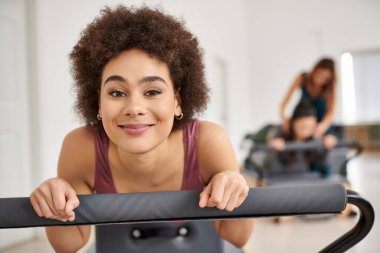 Atletik neşeli kadın pilates dersi sırasında arkadaşıyla arka planda egzersiz yapıyor..