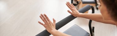 Sportif bir kadın, pilates dersi sırasında kollarını nazikçe bara uzatır..