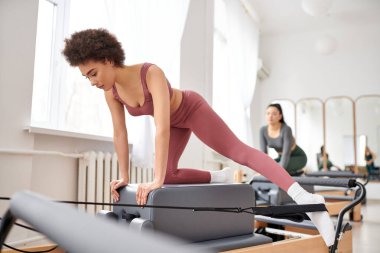 Young women in cozy attire practicing pilates in a gym together. clipart