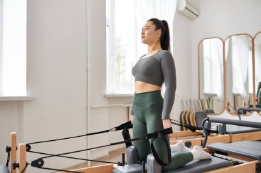 Pilates dersinde spor kıyafetli genç bir kadın antrenman yapıyor..