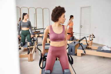 Ekipmanlarla dolu bir spor salonunda spor yapan bir grup kadın..
