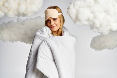 A beautiful blonde woman wrapped in a blanket, surrounded by fluffy clouds. clipart