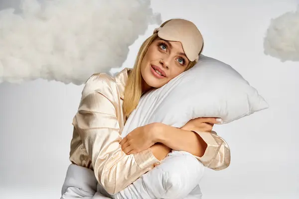 Stock image Blonde woman in cozy pyjamas holding fluffy pillow surrounded by clouds.