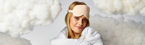 Блондинка в белом одеяле позирует на белом фоне облака.
