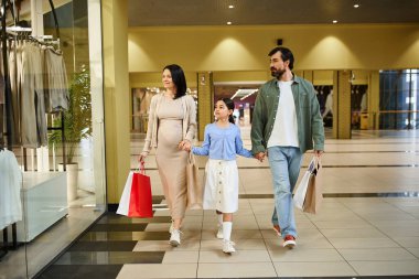 Mutlu bir aile alışverişlerle dolu renkli alışveriş çantaları taşıyan hareketli bir alışveriş merkezinde yürüyor..