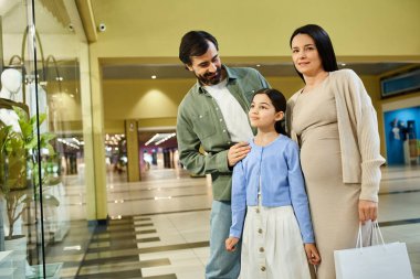Alışveriş torbalarıyla mutlu bir aile, hareketli bir alışveriş merkezinde rahatça geziniyor..